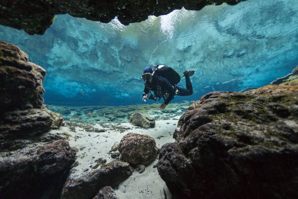 This is a close look at a diver at the bottom of an underwater cave with rocks and boulders.