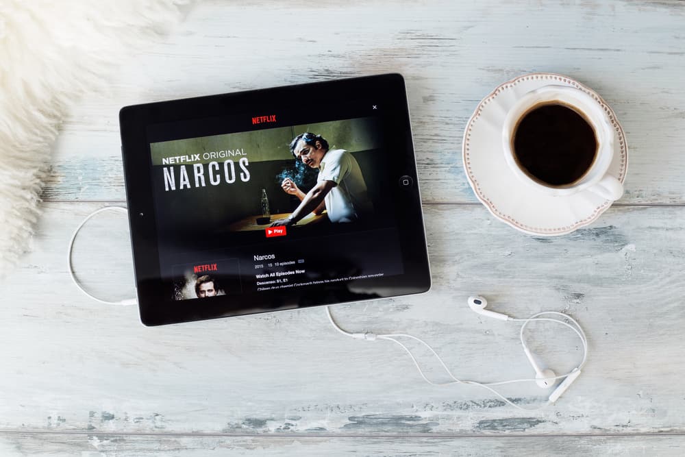 A tablet showcasing the Narcos homepage in Netflix on a table with a cup of coffee.